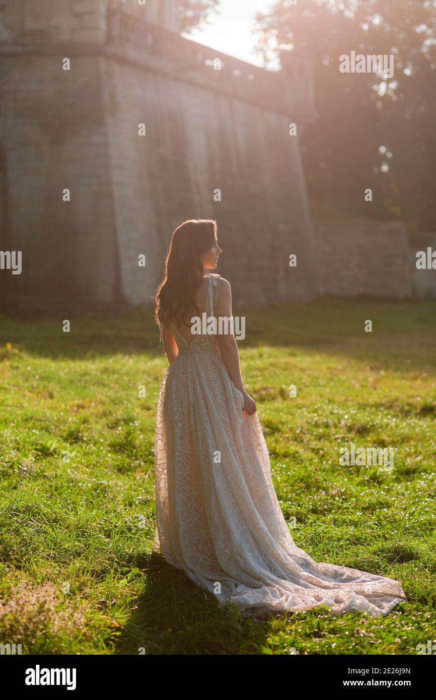 Beautiful bride in the luxurious wedding dress looking to the side in front of old wall at the sunset.. Wedding photo Stock Photo