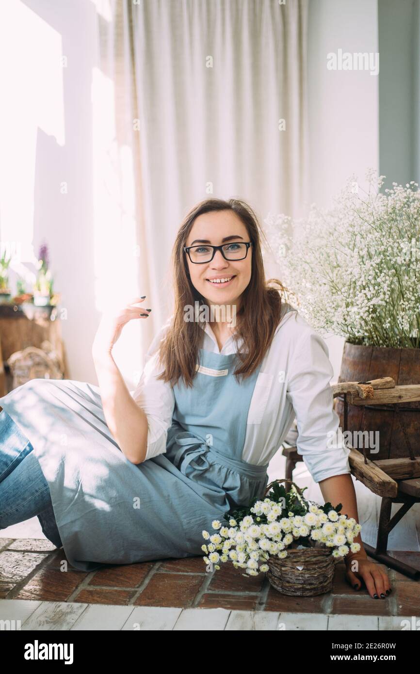Beautiful young girl in an apron among the flower shop. Spring