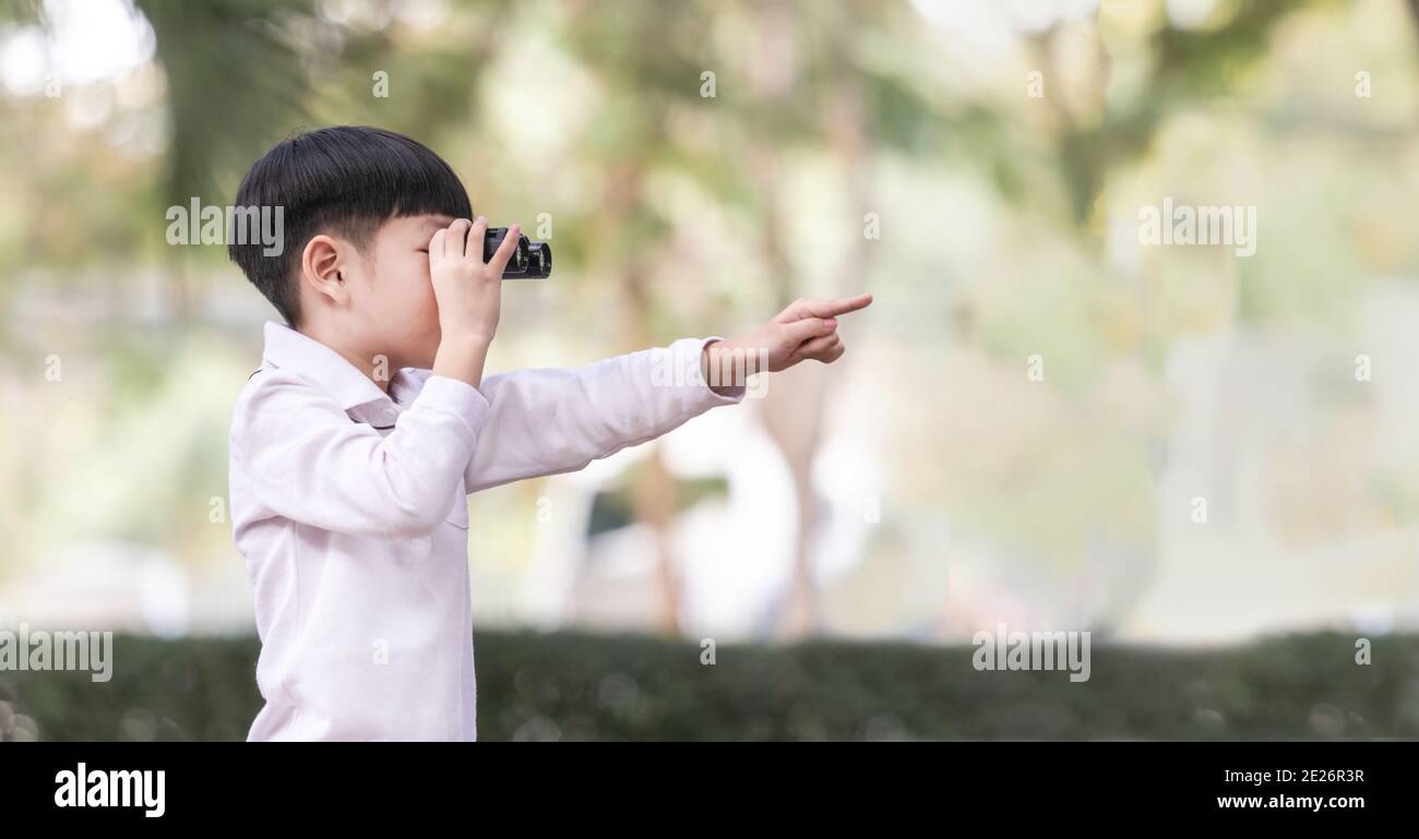 Little Asian boy looking through binoculars in the forest. The child was watching binoculars and pointing the finger forward. Stock Photo