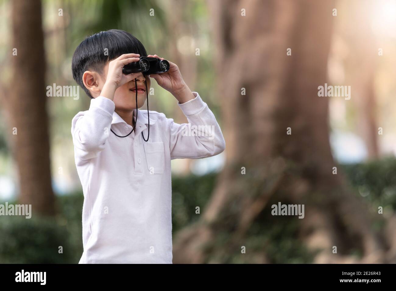 Little Asian boy looking through binoculars in the forest. The child was watching binoculars in nature outdoor. Stock Photo
