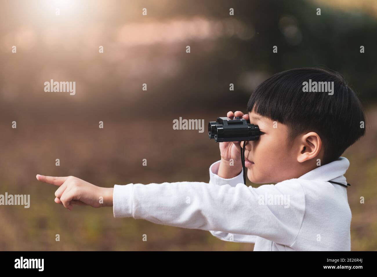 Little Asian boy looking through binoculars in the forest. The child was watching binoculars and pointing the finger forward. Stock Photo