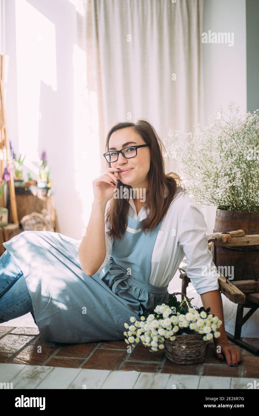 Beautiful young girl in an apron among the flower shop. Spring