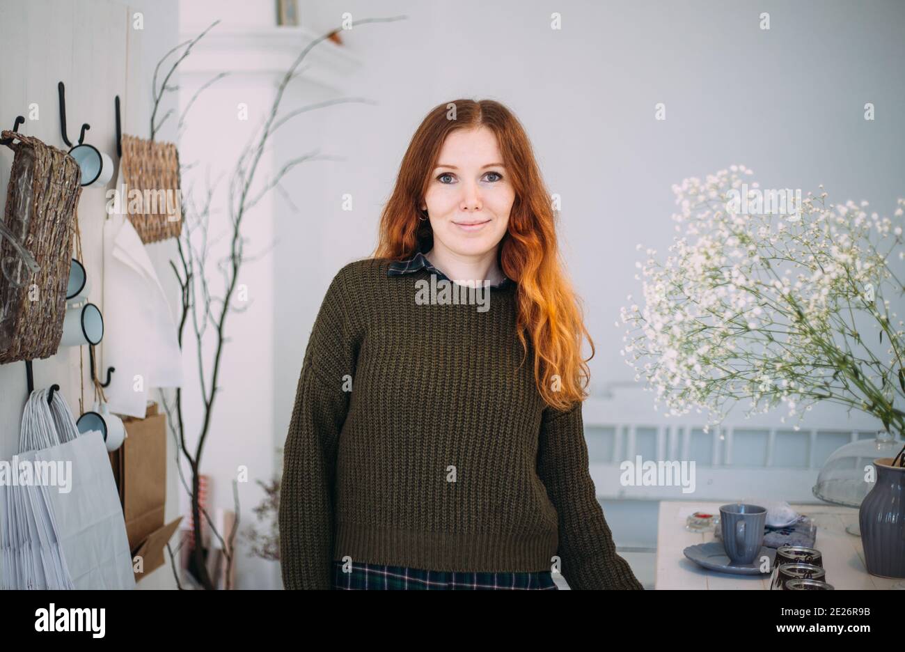 Beautiful ginger young girl in an apron among the flower shop. Spring