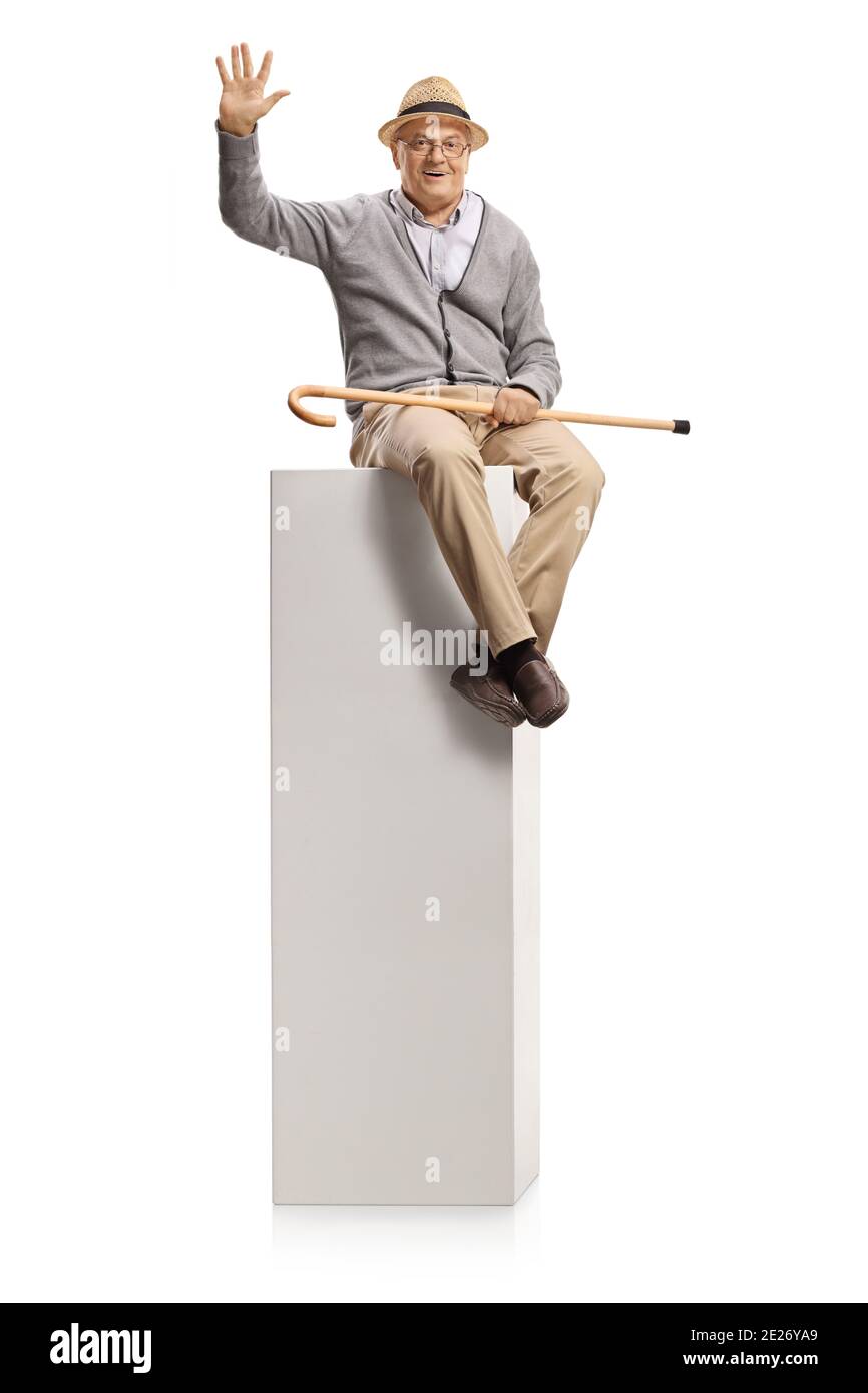 Elderly man with a cane sitting on a white column and waving isolated on white background Stock Photo