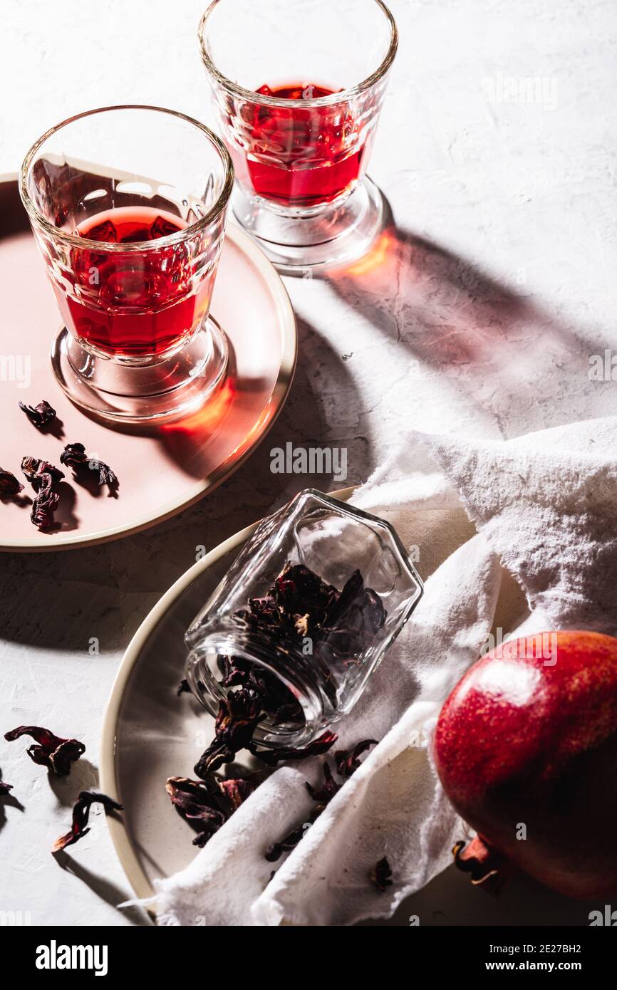 Refreshing fruit herbal tea in glasses, ripe pomegranate on plate, hibiscus tea and dry rose petals, hard light with harsh shadows Stock Photo