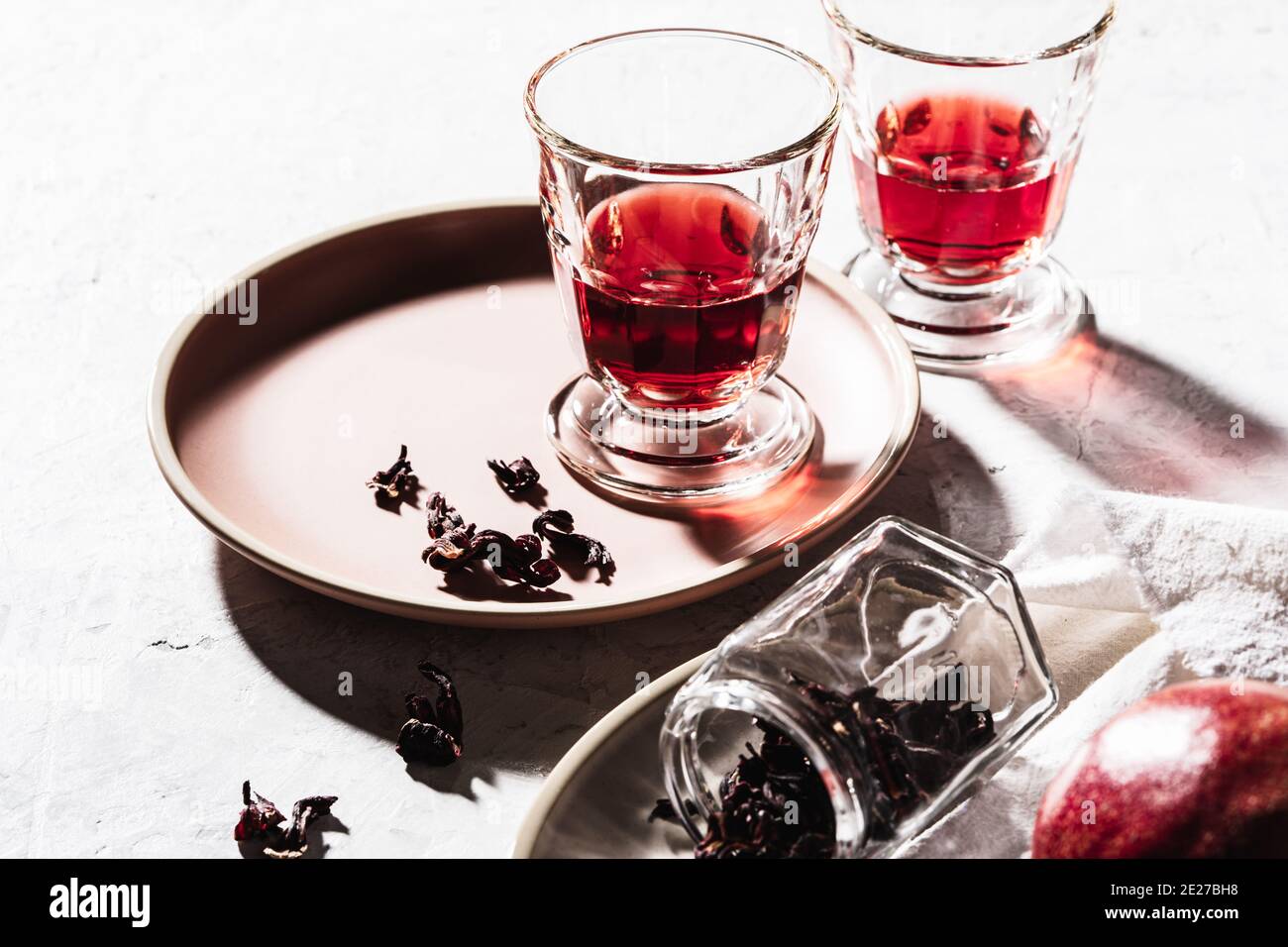 Refreshing fruit herbal tea in glasses, ripe pomegranate on plate, hibiscus tea and dry rose petals, hard light with harsh shadows Stock Photo