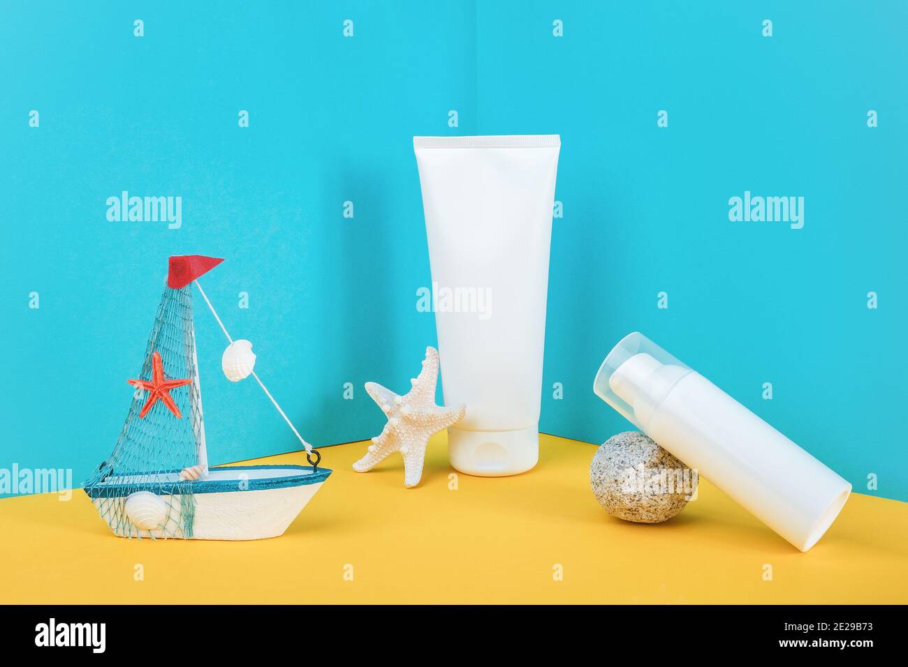 White blank cosmetic tube, bottle with sunscreen, sun cream, moisturizing lotion, starfish, rock and small boat on blue, yellow background. Concept sk Stock Photo