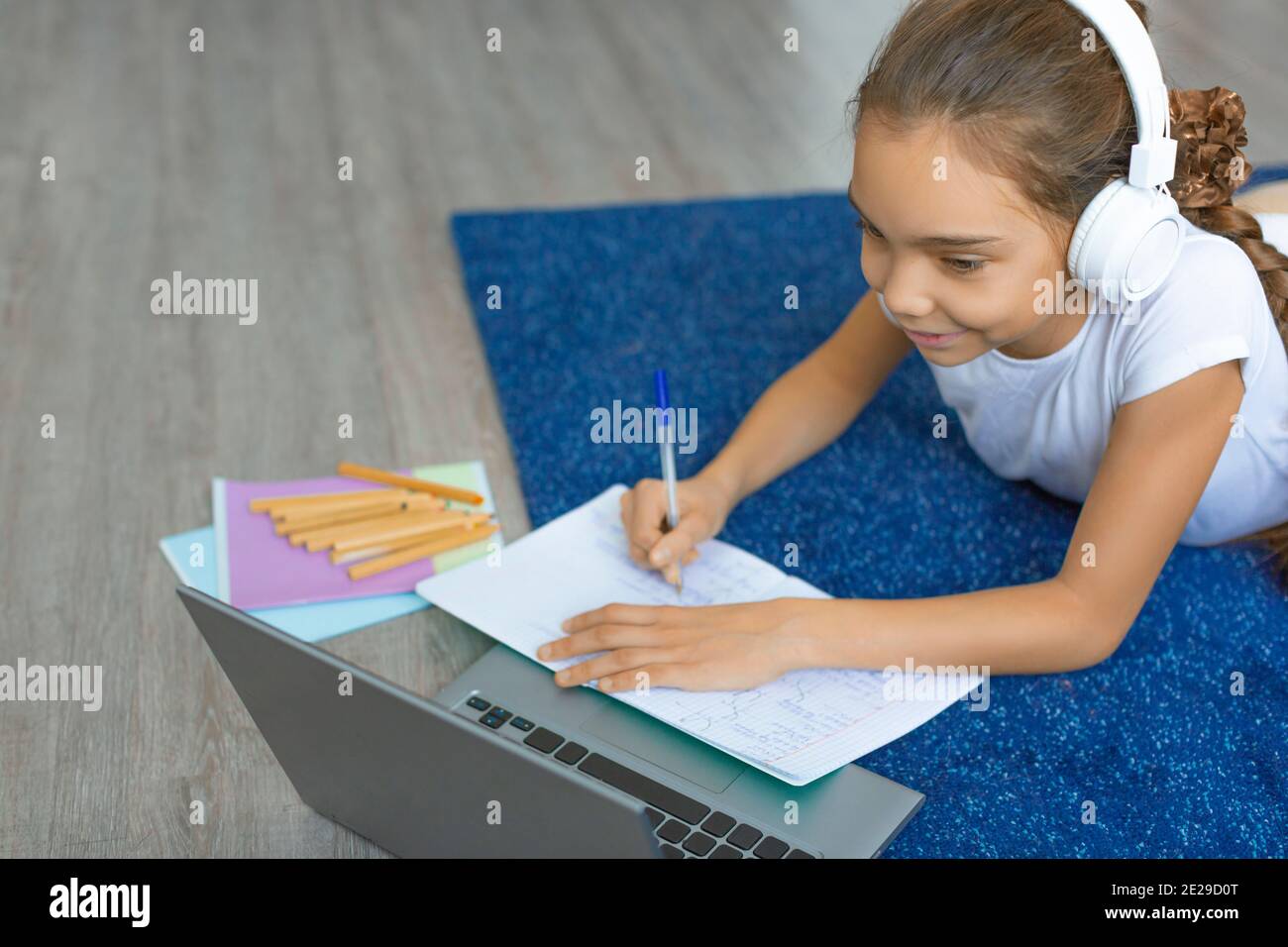Top view of a pupil girl doing homework on the floor at home in front ...