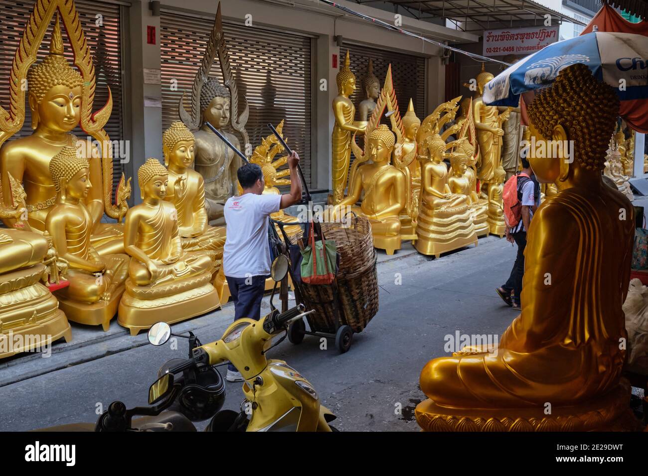 A man with a pushcart passes Buddha statues in front of a factory for Buddha statues in Bamrung Muang Road, Bangkok, Thailand Stock Photo