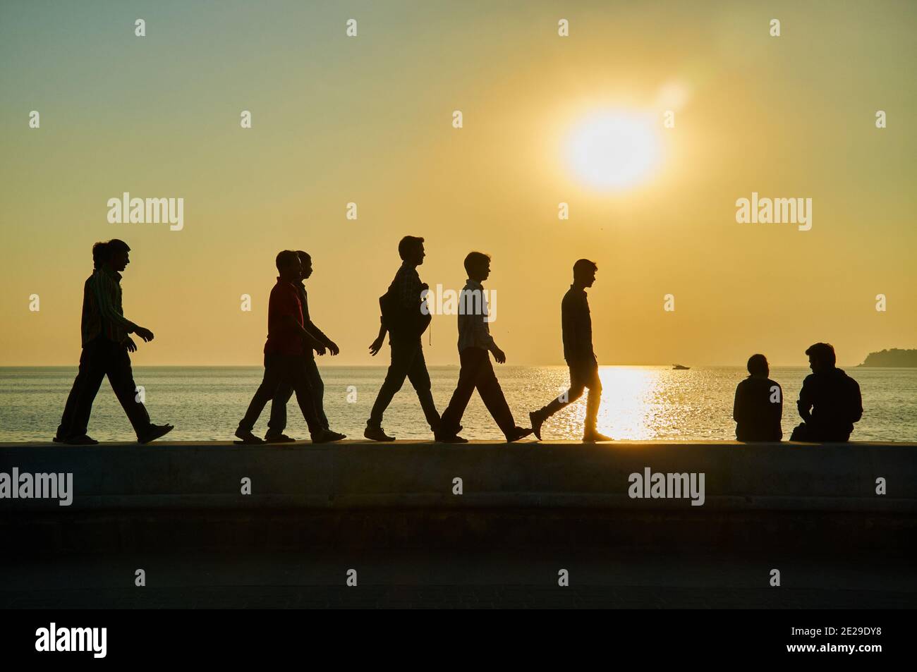 Silhouettes of sightseers, in the late afternoon sun walking on the embankment wall by the Arabian Sea at Marine Drive, Mumbai, India Stock Photo