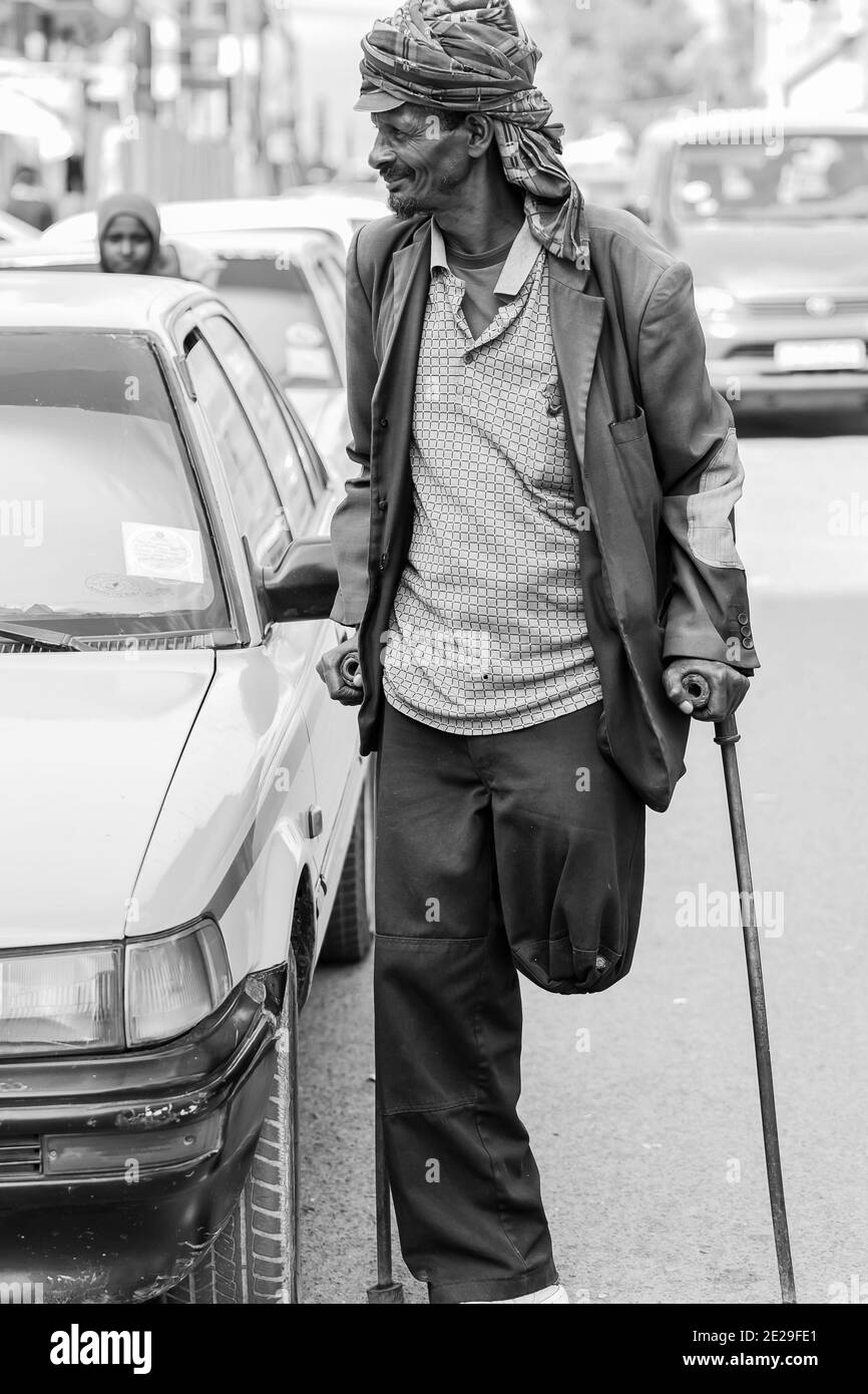 ADDIS ABABA, ETHIOPIA - Jan 05, 2021: Addis Ababa, Ethiopia, January 27, 2014, Old Arabic man using crutches next to a yellow taxi in quiet city stree Stock Photo