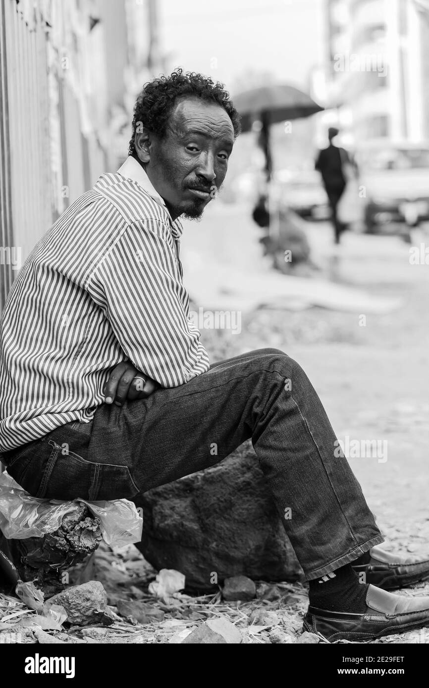 ADDIS ABABA, ETHIOPIA - Jan 05, 2021: Addis Ababa, Ethiopia, January 27, 2014, African man sitting on the street corner looking straight at camera Stock Photo