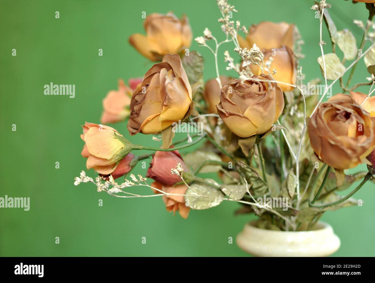 A flower white vase with a bouquet of autumn brown colored artificial roses on green background with side lightening. Front view, copy space Stock Photo