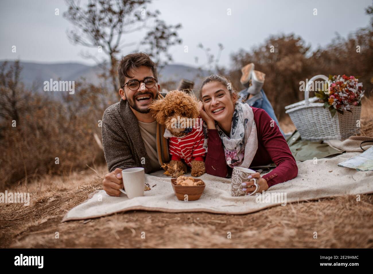 Couple at picnic plying on blanket with their dog and drinking tea ...