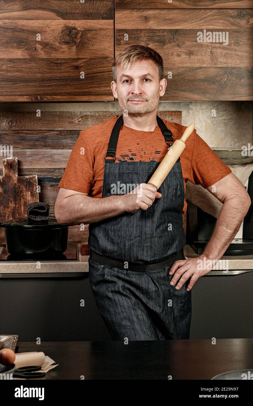 Caucasian man is cooking. Stylish baker 45 years old in a apron with rolling pin in a home kitchen. Cook at home. Life style photography. Vertical sho Stock Photo