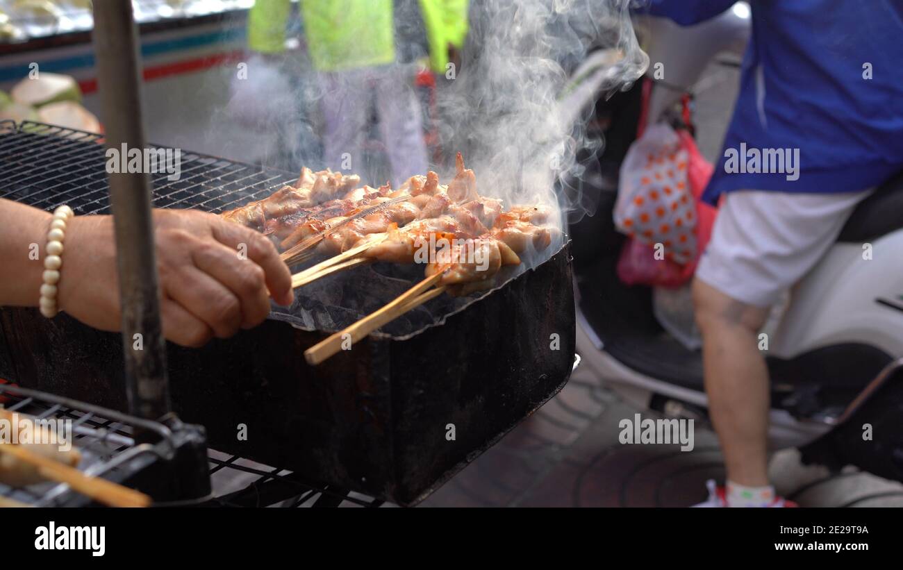 Grilled chicken with wooden stick on charcoal grill at street market in Bangkok, Thailand. Stock Photo
