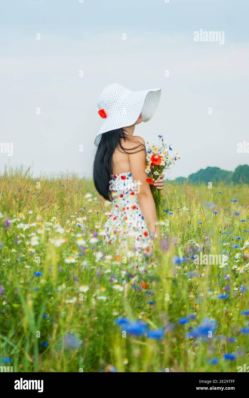 Girl in a dress and a white hat stands in a field with a bouquet of ...