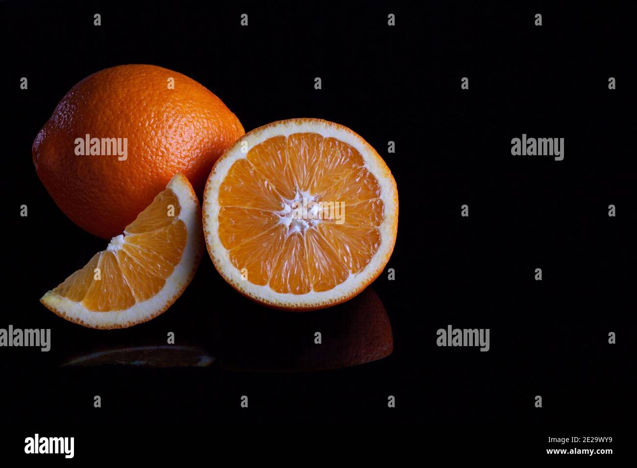 Ripe orange fruit sliced coposition on a black reflective background Stock Photo