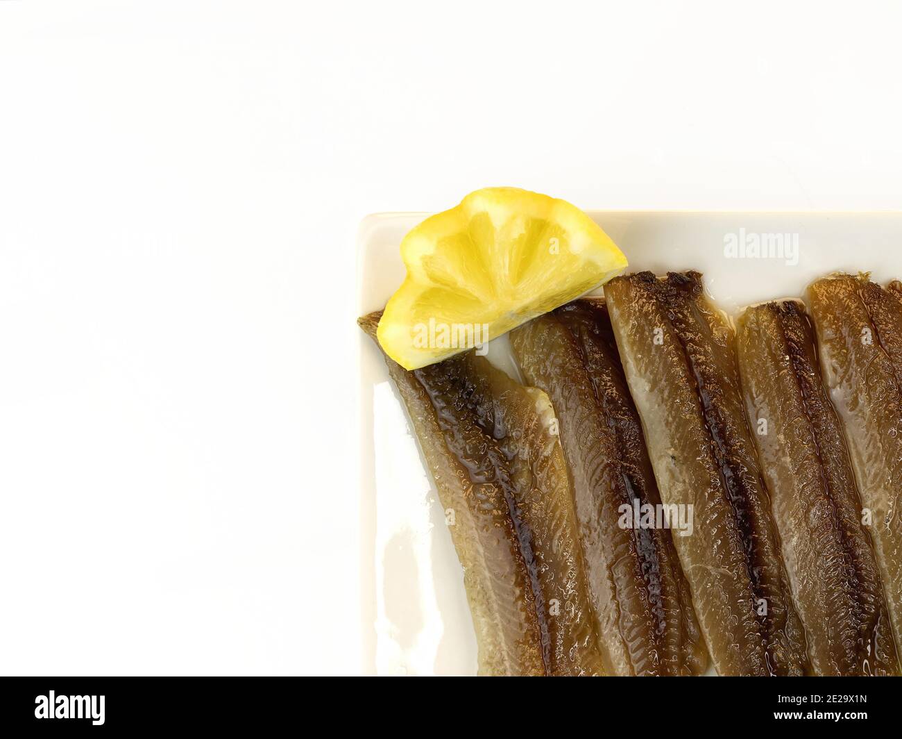 Salted sardines canned with olive oil on a plate with a lemon wedge