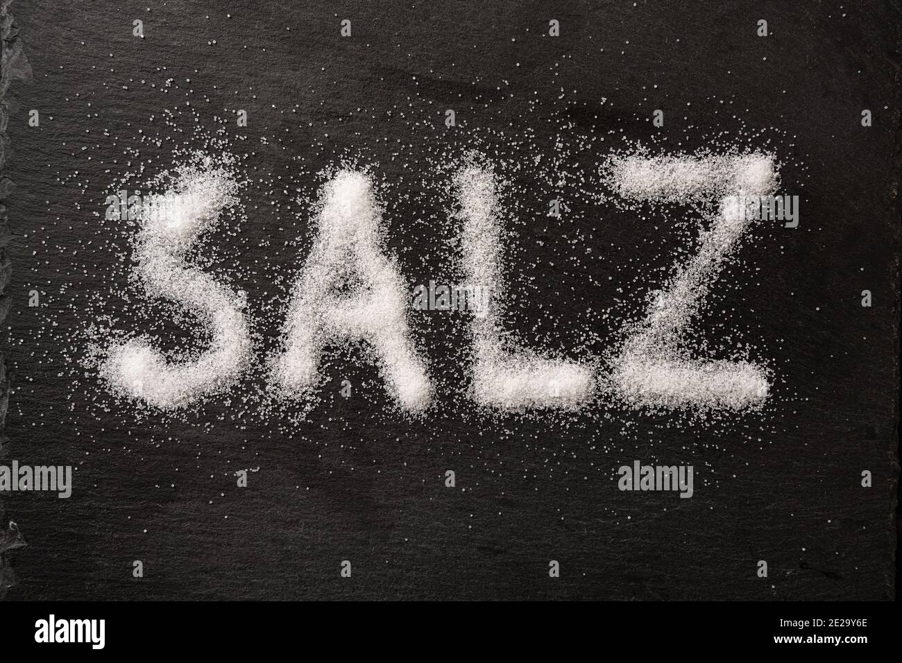 German word Salz (meaning salt) written with salt crystals on a dark slate, high angle view from above, selected focus Stock Photo