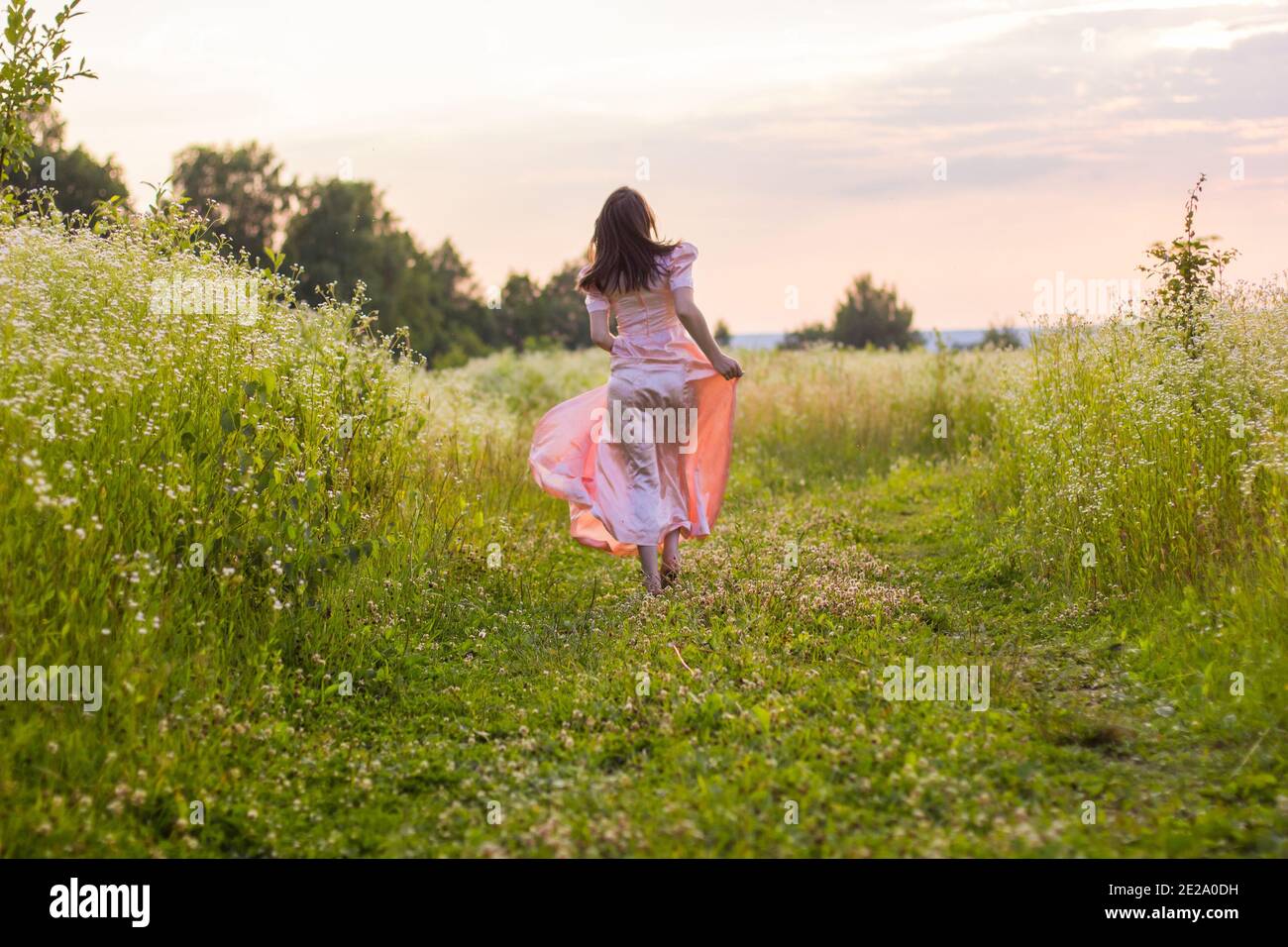 girl running across the field in a pink dress Stock Photo
