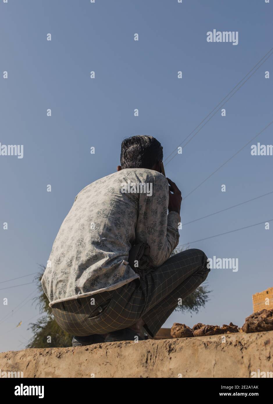 Jaisalmer, Rajasthan / India - January 8 2020 : man sitting on a wall does multitask, talking to mobile phone smoking cigarette looking at the photogr Stock Photo