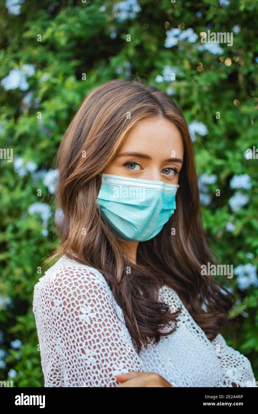 Shallow focus of an adult brunette female wearing a lace shirt with facemask and posing outdoors Stock Photo