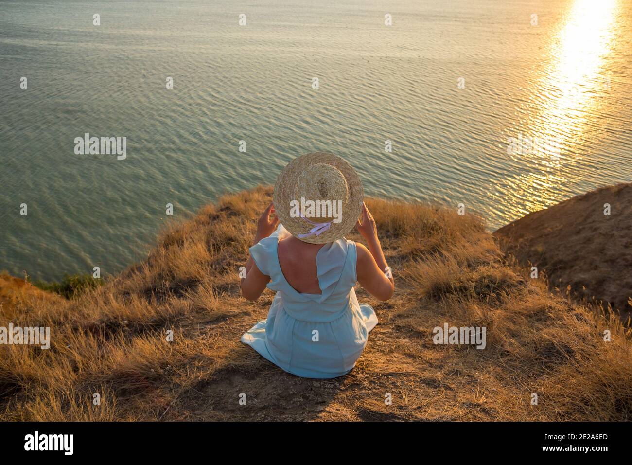 A girl in a dress and hat sits on a cliff by the sea Stock Photo - Alamy