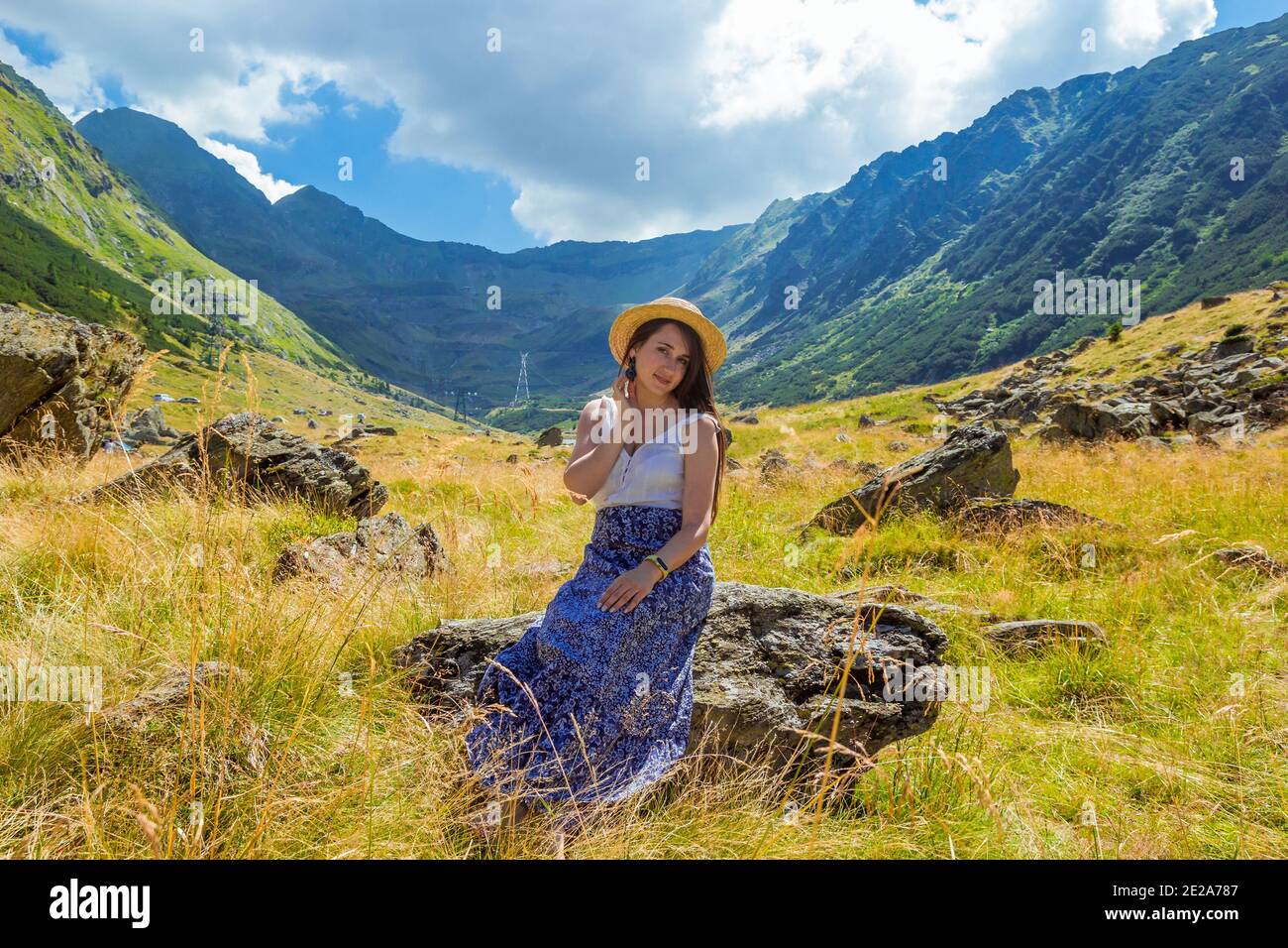 girl in dress and hat sits on a rock against the background of high ...