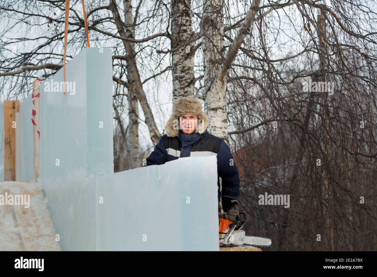 A slinger in a hat with light fur in a blue winter jacket assembling ice panels of an ice town Stock Photo