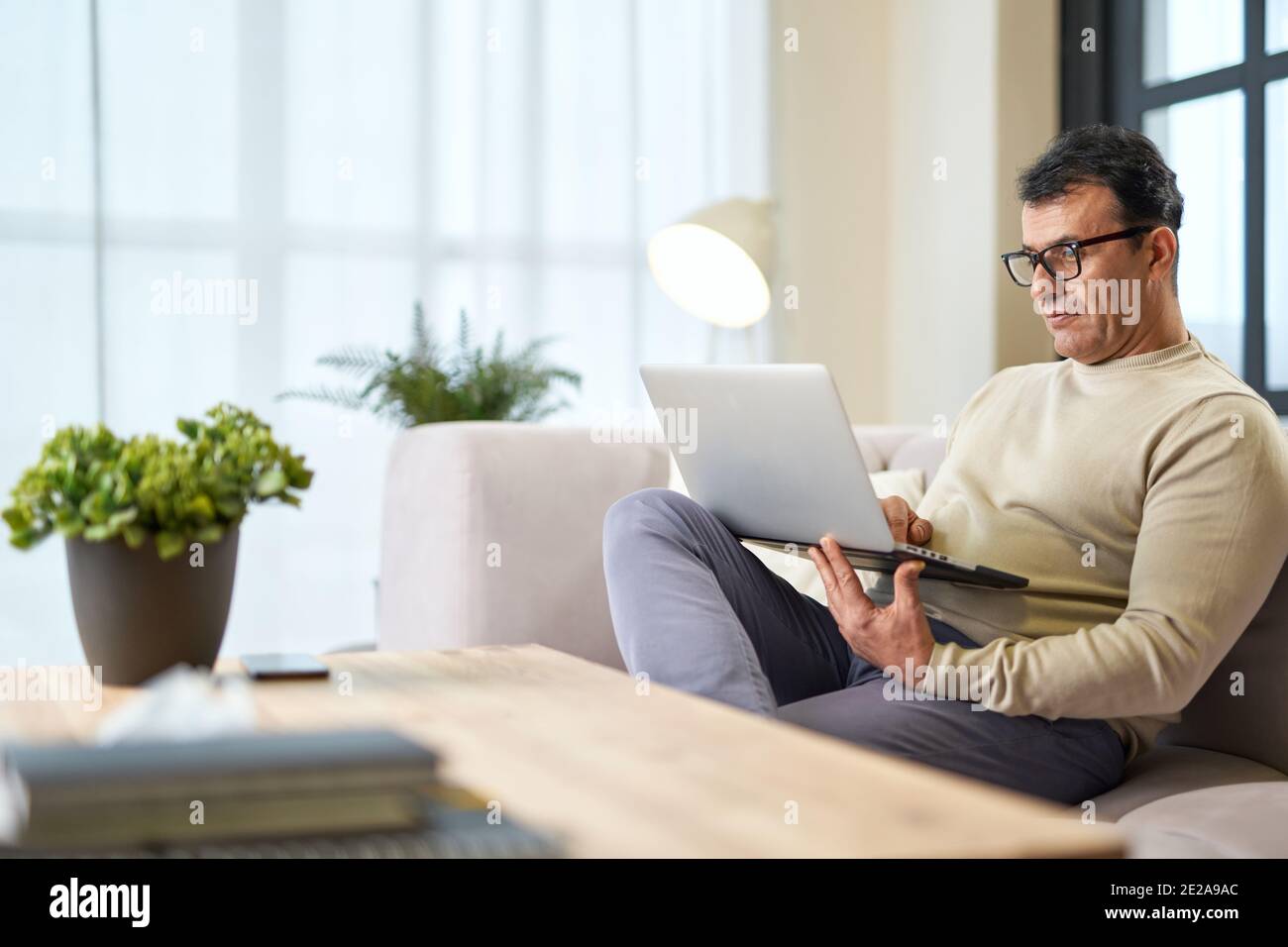 Handsome latin middle aged businessman in eyeglasses using laptop while working from home. Telework, business concept Stock Photo