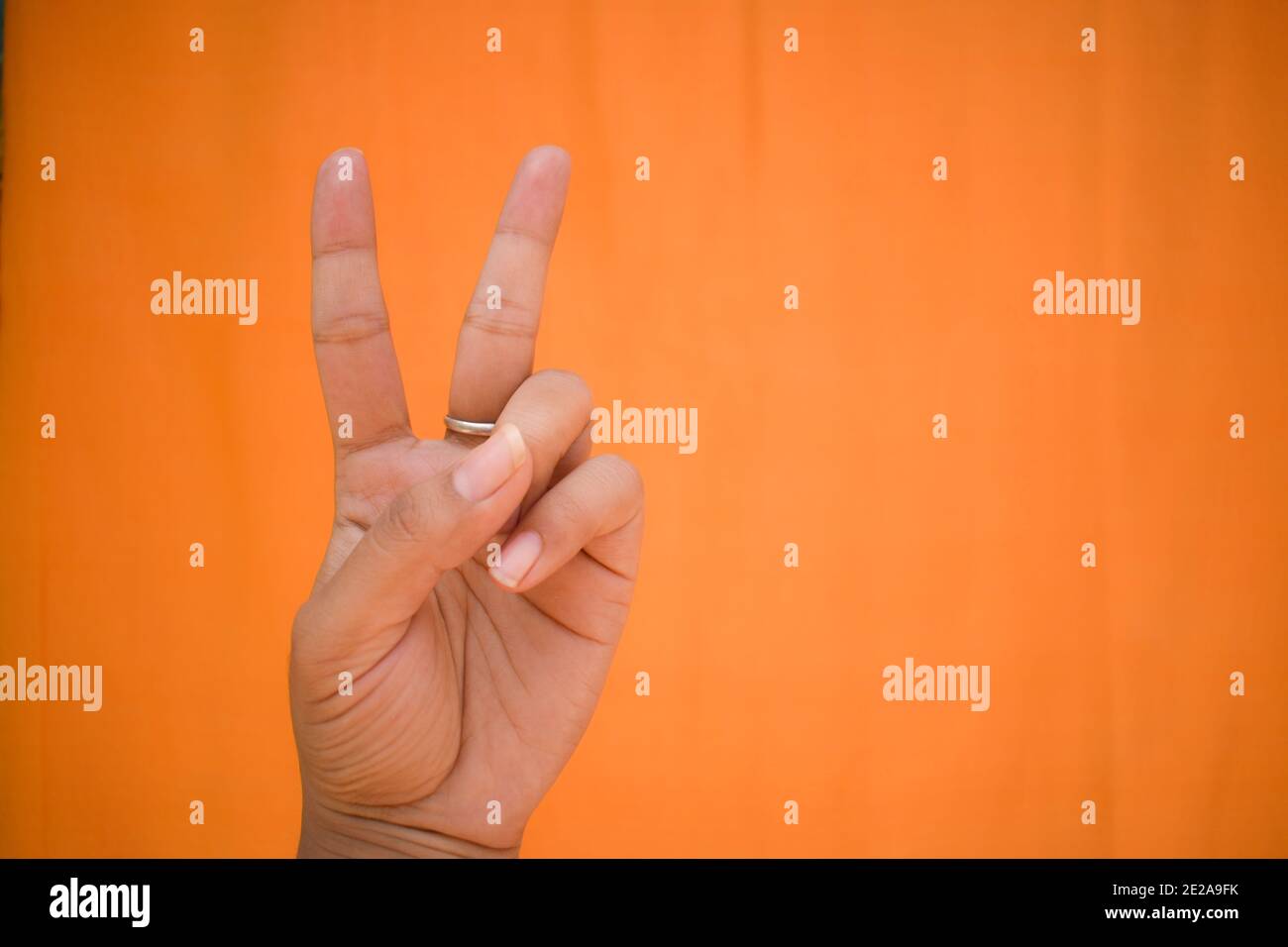 Hand showing victory sign against an orange background Stock Photo