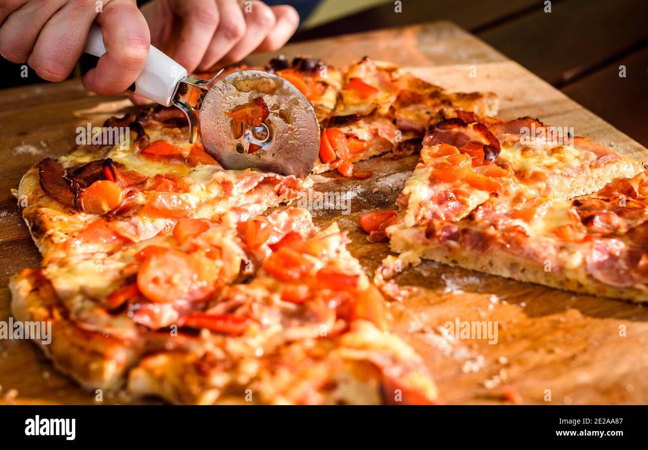 Making of homemade Italian pizza in fireplace brick oven. Making of traditional pizza in stone brick fireplace with fire wood and coals. Cutting finis Stock Photo