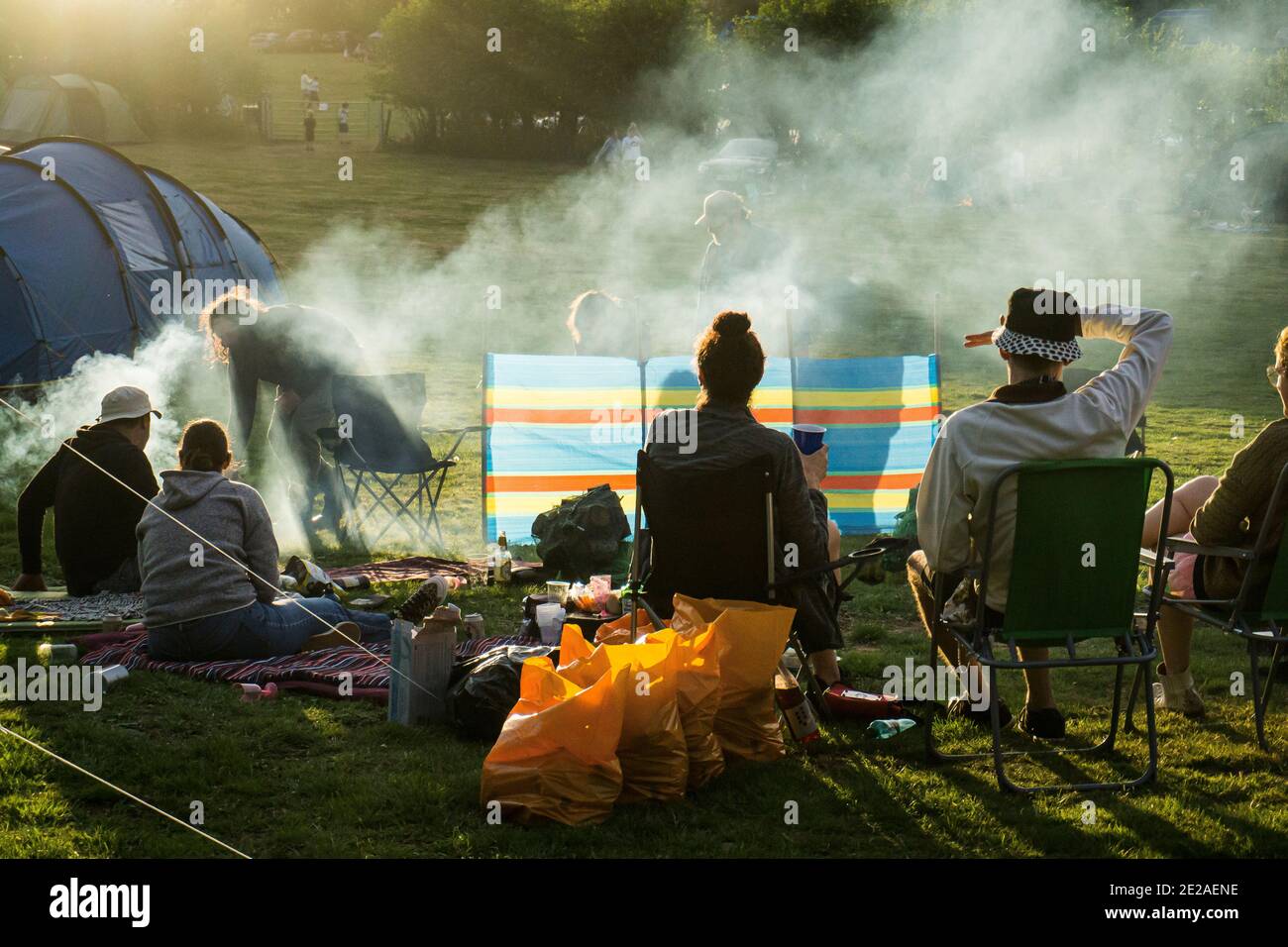 Group of friends at a campsite, preparing a very smokey barbecue at sundown Stock Photo