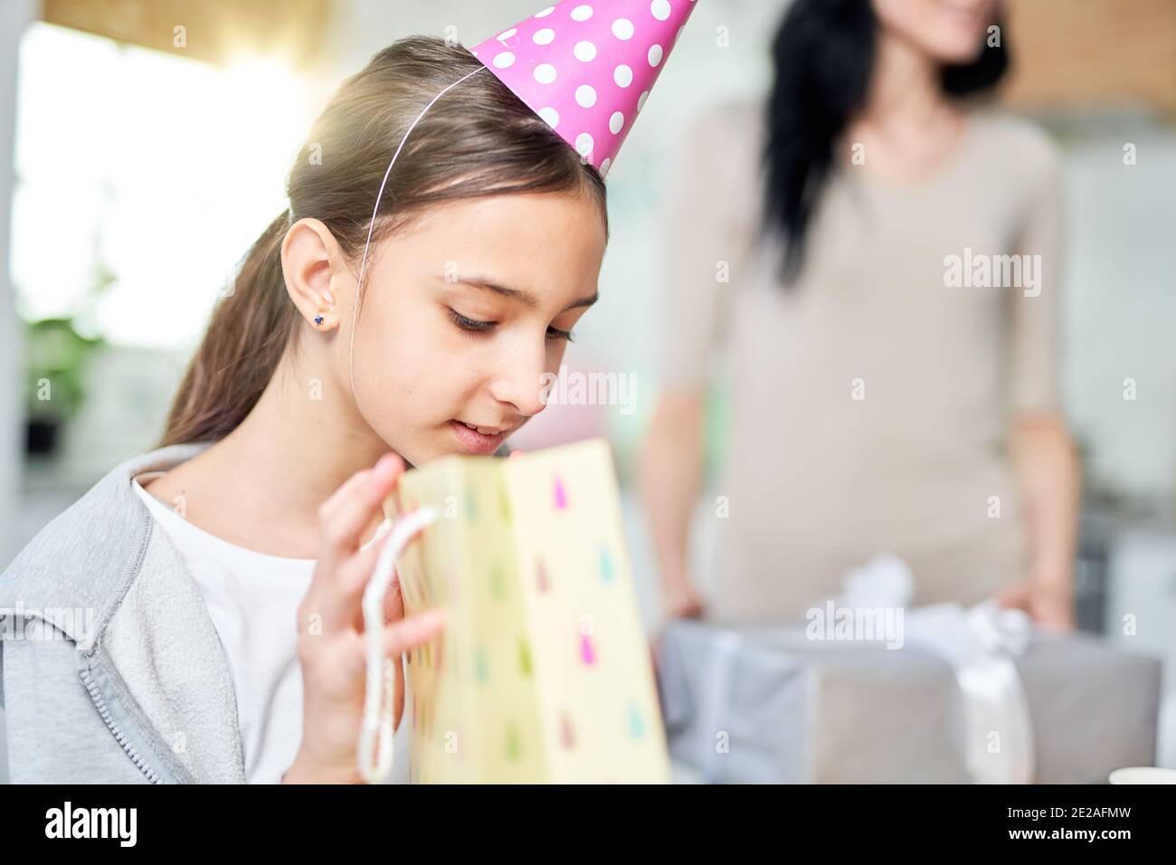 Portrait of curious teenaged latin girl checking gift bag, while receiving presents, celebrating birthday with parents at home. Celebration, childhood concept Stock Photo