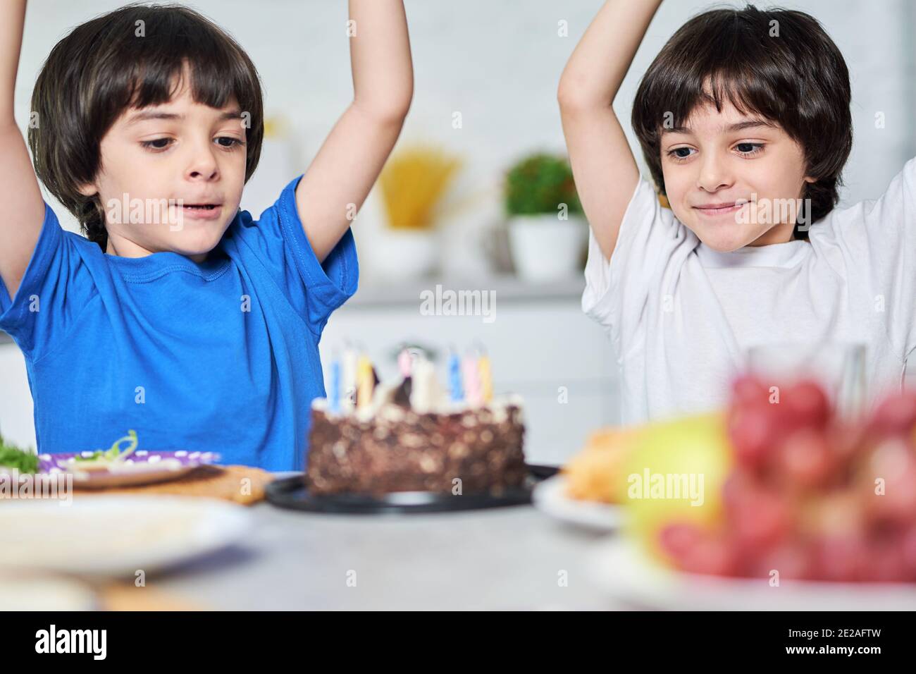 Excited little hispanic twins looking happy after blowing candles on a birthday cake. Children celebrating birthday together with parents at home. Selective focus on kids Stock Photo