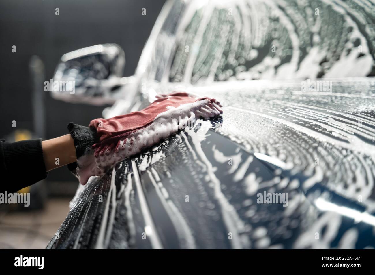 Professional car wash. Detailing worker washes the vehicle body with