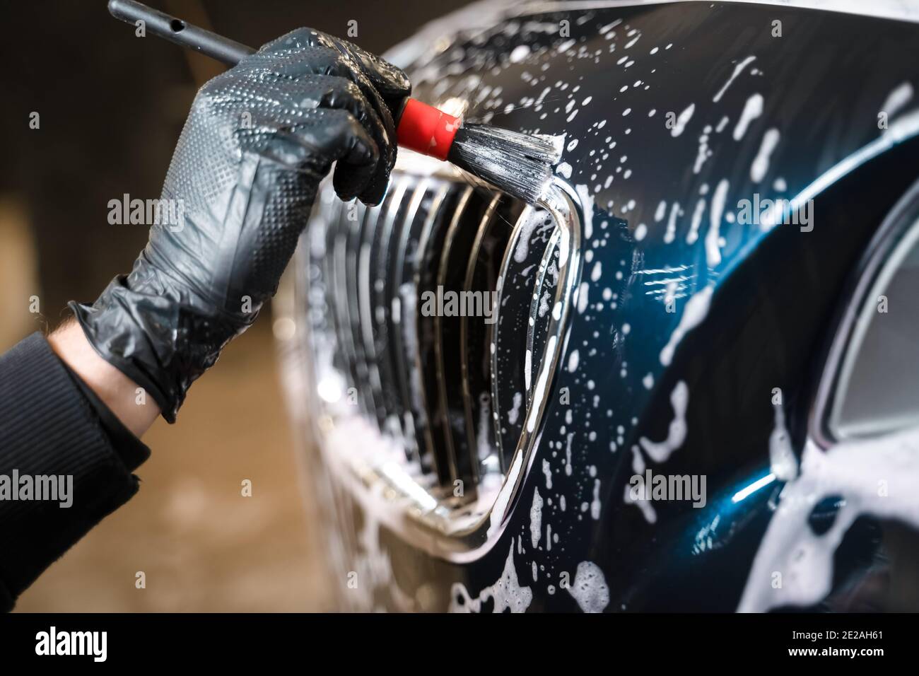 Detailed car wash. Detailing center worker cleans car's radiator grill with brush Stock Photo