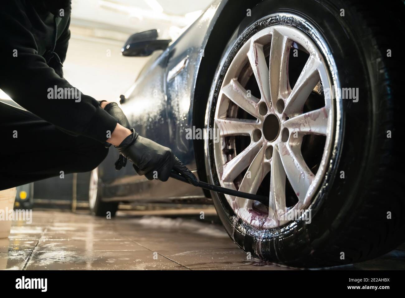 Detailing center worker cleans car wheels with brush. Vehicle wheel rim