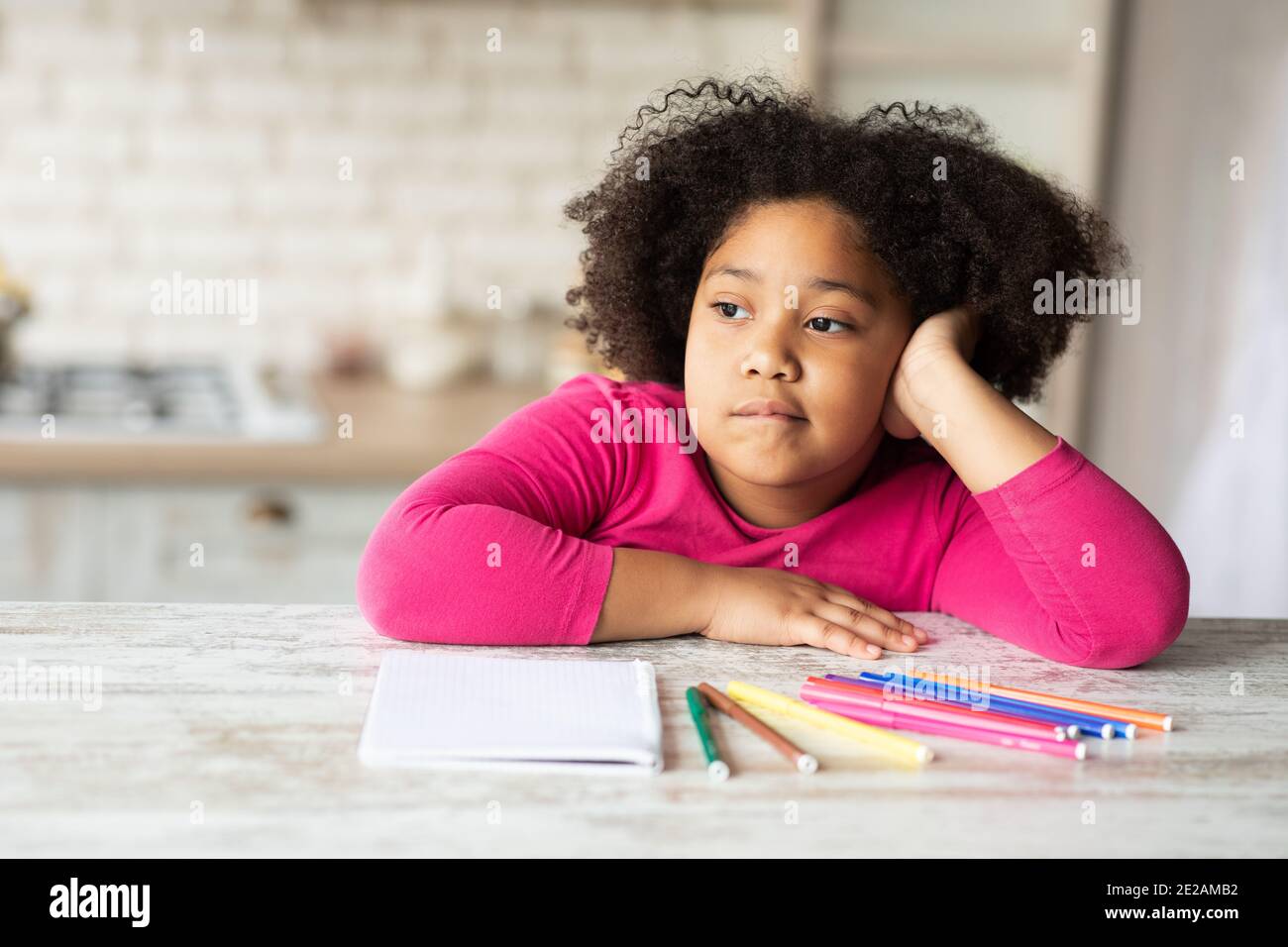 Boredom. Cute little bored black girl sitting at table in kitchen Stock Photo