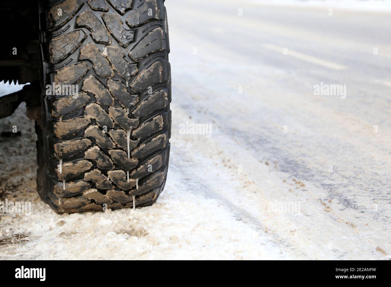 Car wheel covered with icicles and mud on a snowy road. Winter tires
