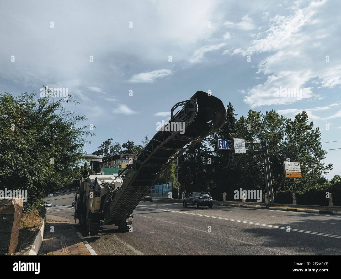 Russia, Sochi 05.07.2020. A road milling machine stands on the side of road with cars passing by, green trees and the sky Stock Photo