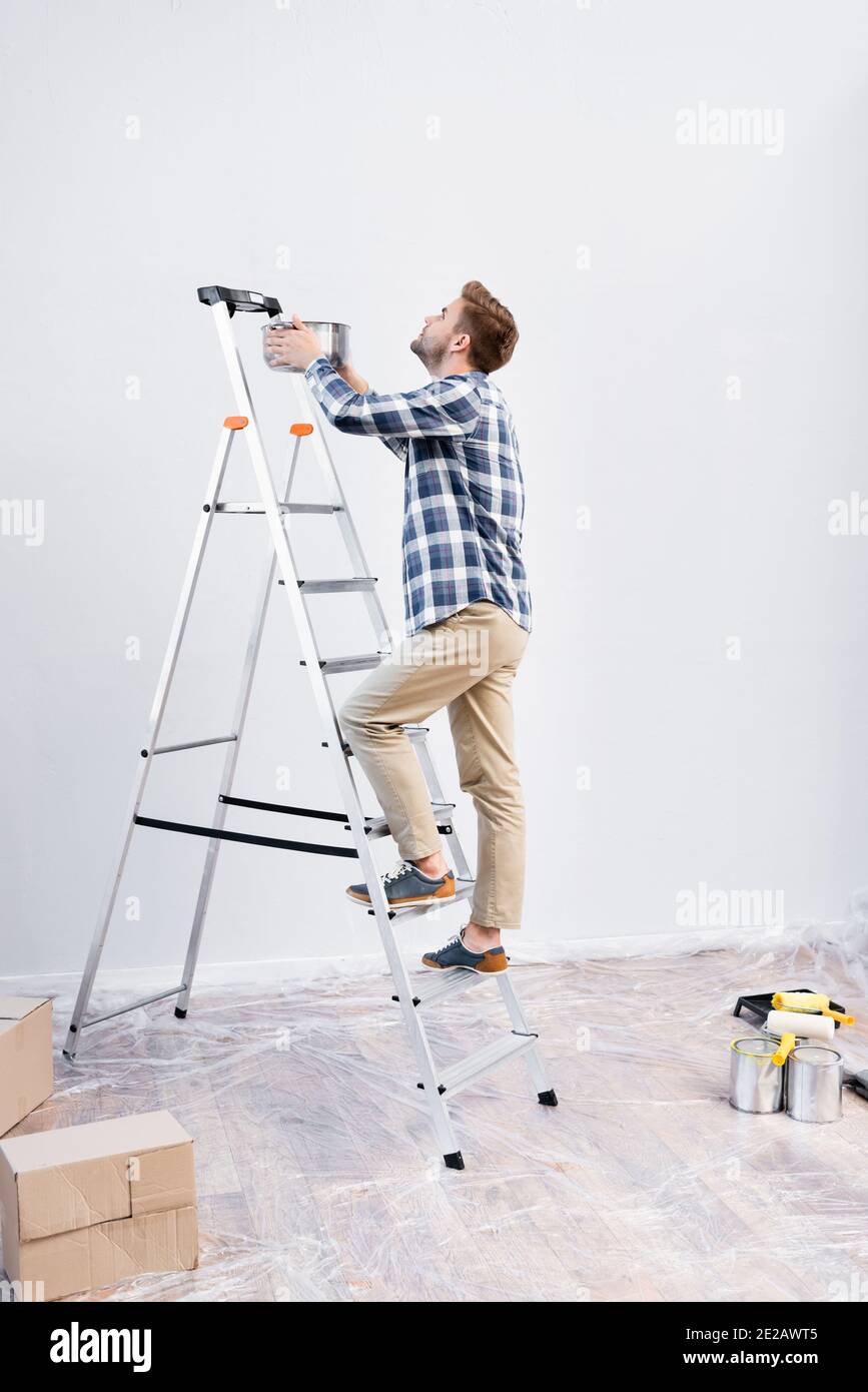 full length of young man with pot standing on ladder under leaking ceiling at home Stock Photo
