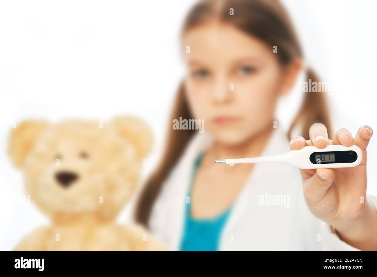 Sad child holding an electronic thermometer in the foreground. Girl has a fever, flu, and high body temperature Stock Photo
