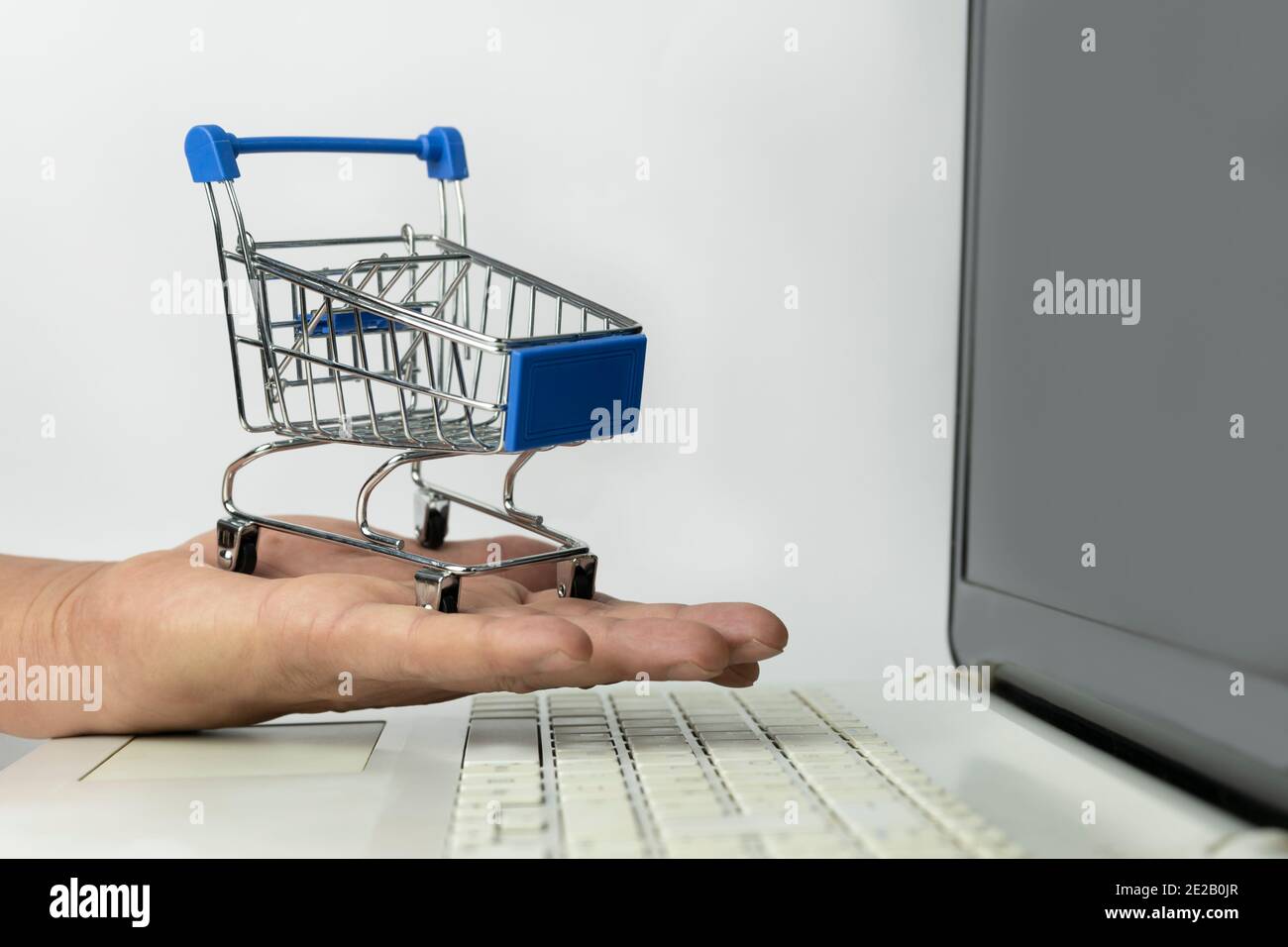 Shopping online concept lifestyle.Hand holding mini shopping cart trolley on laptop.E-commerce ,online working business ,spend money mock up template Stock Photo