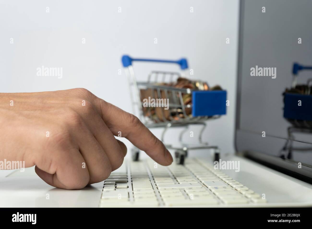 Online shopping e-commerce concept.Man hand using laptop with mini shopping cart full of money coins on background.Business financial spend money life Stock Photo
