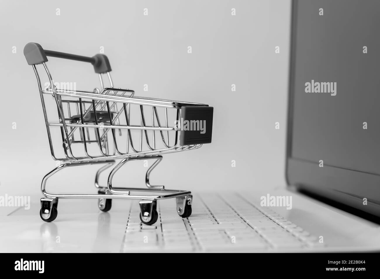 Black and white online shopping concept background. Shopping cart trolley empty on laptop keyboard.E-commerce template mock up with copy space. Stock Photo