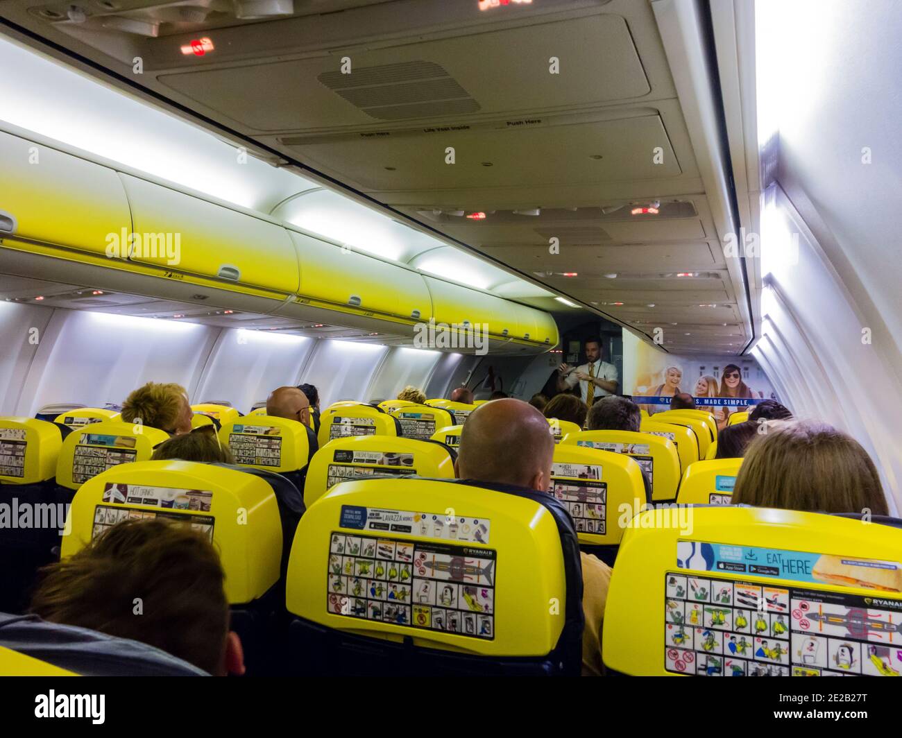 Interior of cabin on a Ryanair Boeing 737-800 passenger jet with steward giving safety instructions before the flight. Stock Photo