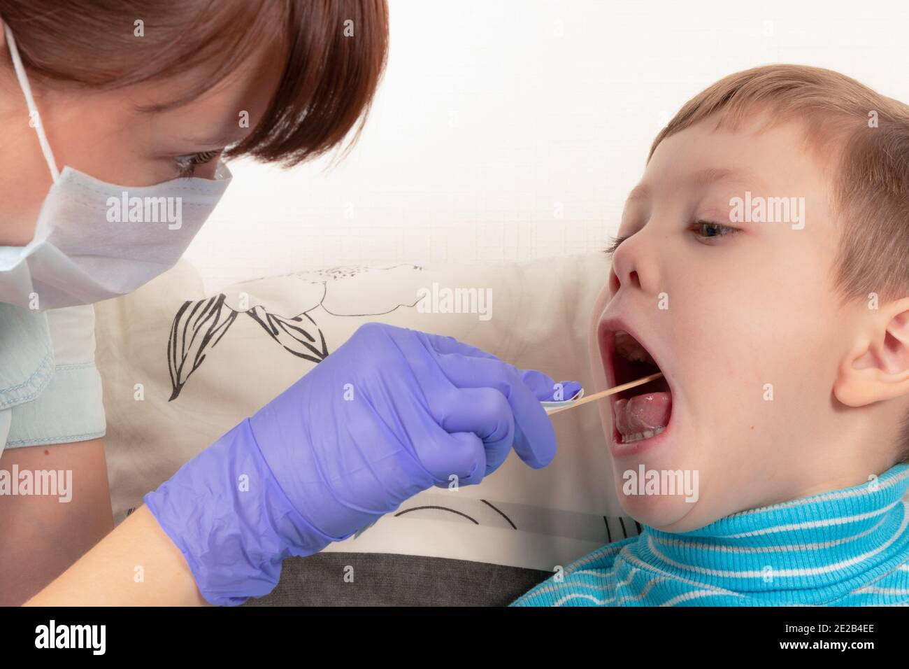 girl doctor in blue medical gloves and a mask examining the throat of a sick child boy Stock Photo