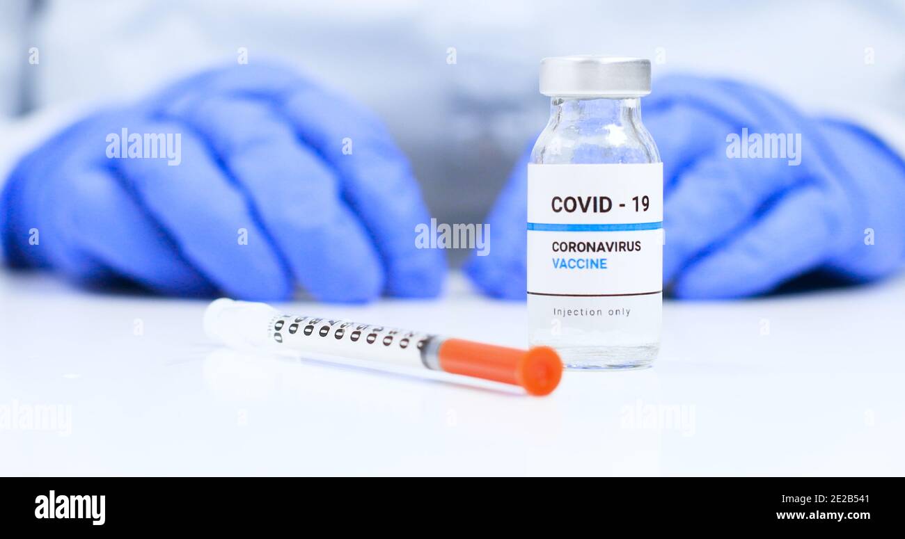 Corona virus Sars-Cov-2 vaccine concept. Doctor hands in blue medical gloves with transparent liquid coronavirus vaccine bottle and syringe for injection in the laboratory. Research and development of new cure for diseases Stock Photo